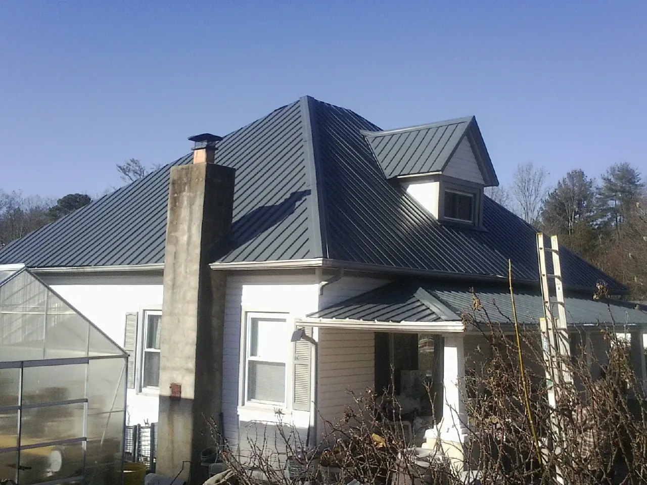 Dark blue standing seam metal roof on a white farmhouse with dormer — Slate & Tile Roof Repair by Roofing Brothers in Arriba