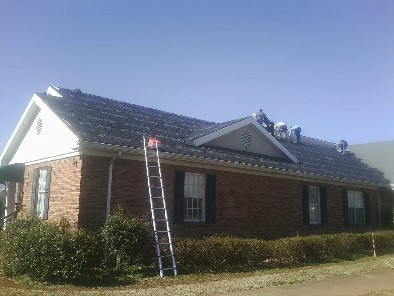Crew tearing shingles off a brick ranch roof with a ladder set — Metal Roof Repair work by our crew in Arriba
