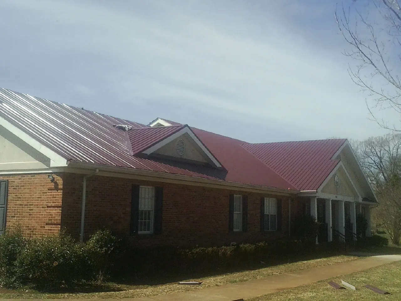 Red metal roof with gabled entries on a long brick building, from a Hail Damage Roof Repair job in Arriba