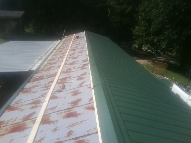 Old rusted panels beside newly installed green metal roofing — Wind Damage Roof Repair by Roofing Brothers in Arriba