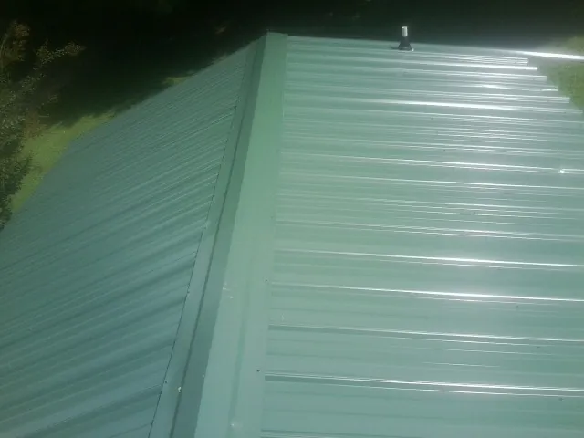 New green metal panels meeting at the ridge of a roof — Flat Roof Repair work by our crew in Arriba