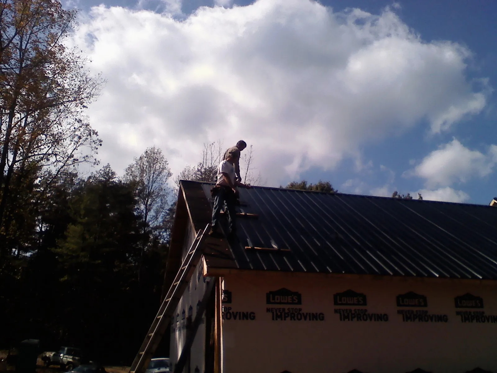Roofer fastening dark metal panels high against a cloudy sky, from a Roof Inspection job in Arriba