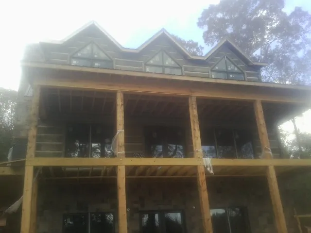 Dormers and porch framing on a large log home under construction — Roof Coating work by our crew in Arriba