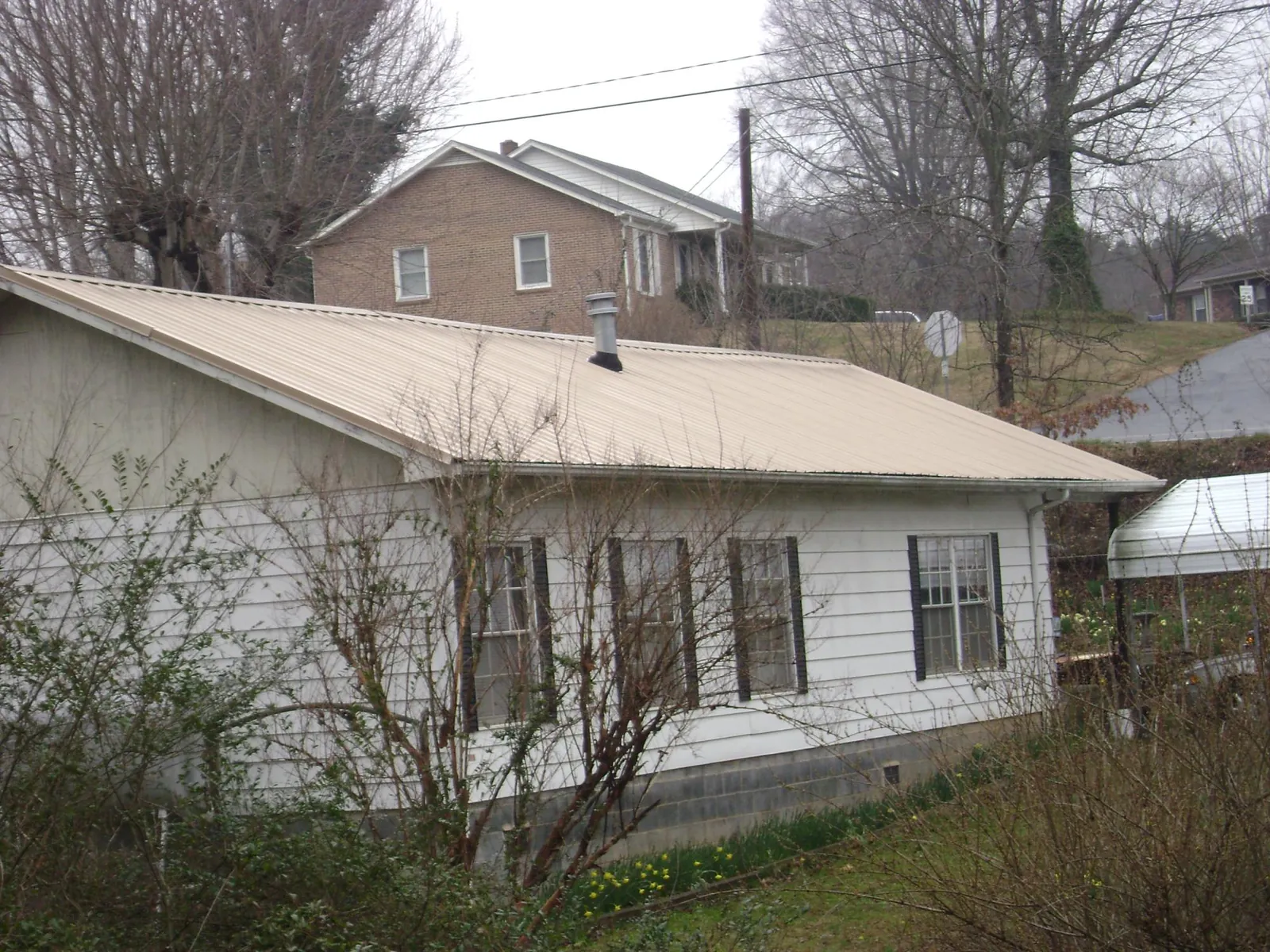 Tan metal roof on a white sided house set into a hillside — Commercial Roofing by Roofing Brothers in Arriba