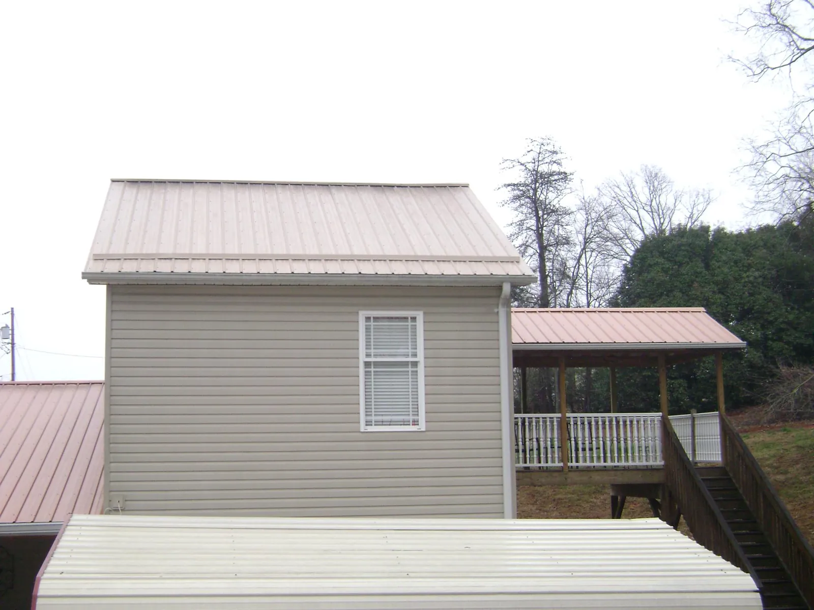 Tan metal roofs on a two story addition and attached porch, from a Roof Replacement job in Arriba